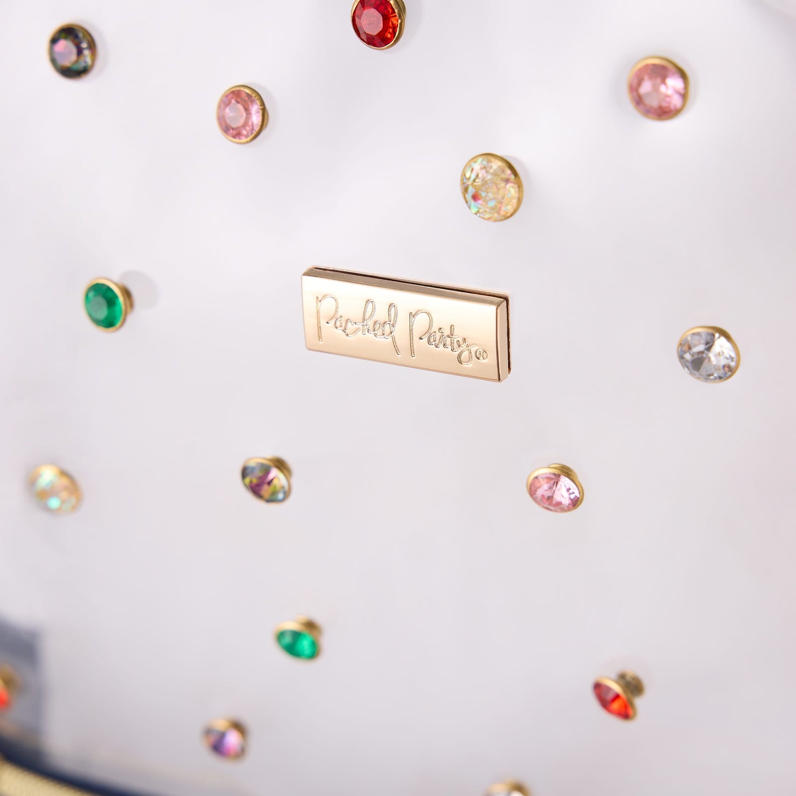 Close-up of colorful gemstone rivets and the Packed Party logo on the Clear Denim and Gems Backpack.