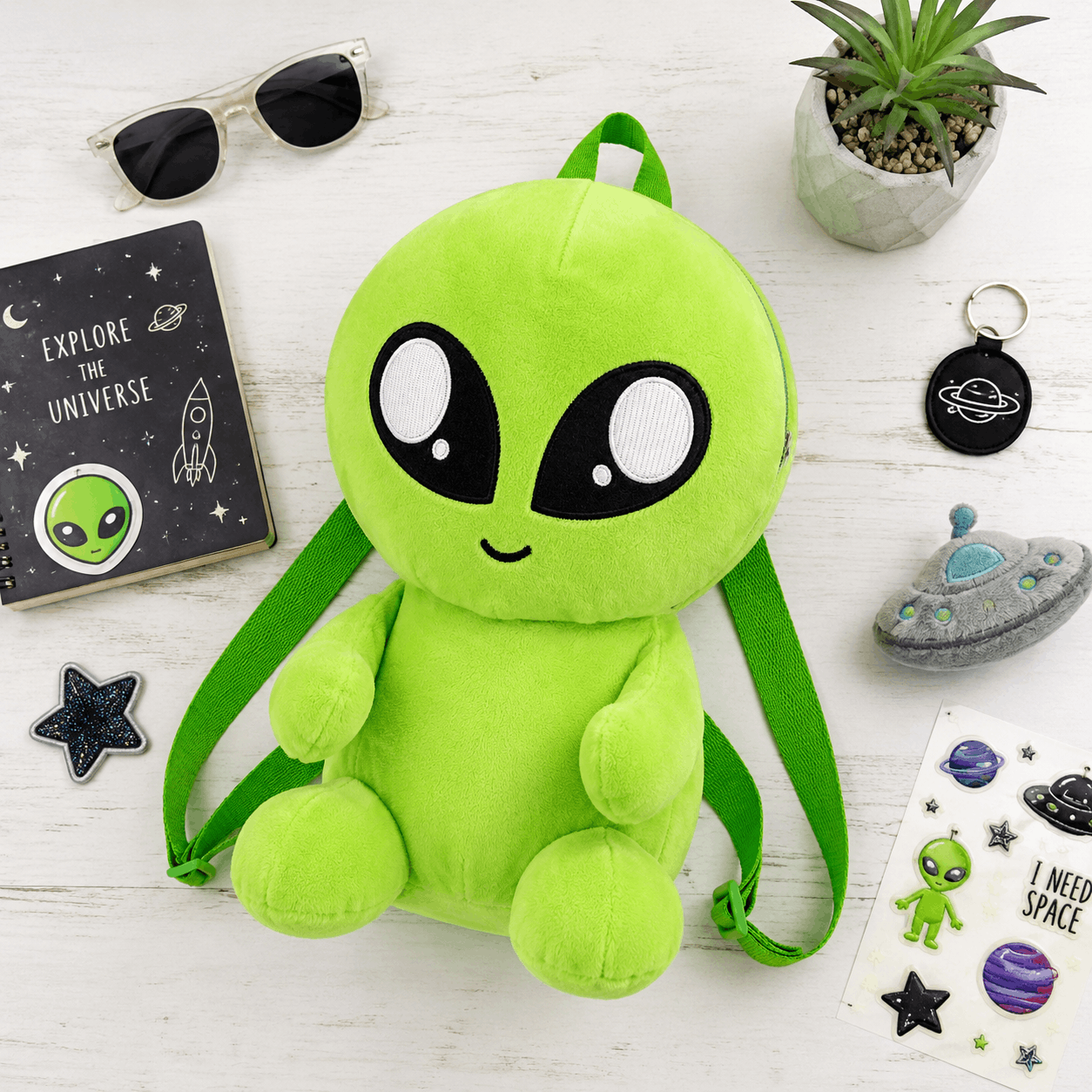 Plush Baby Alien Mini Backpack displayed in a playful flat lay with space-themed accessories.