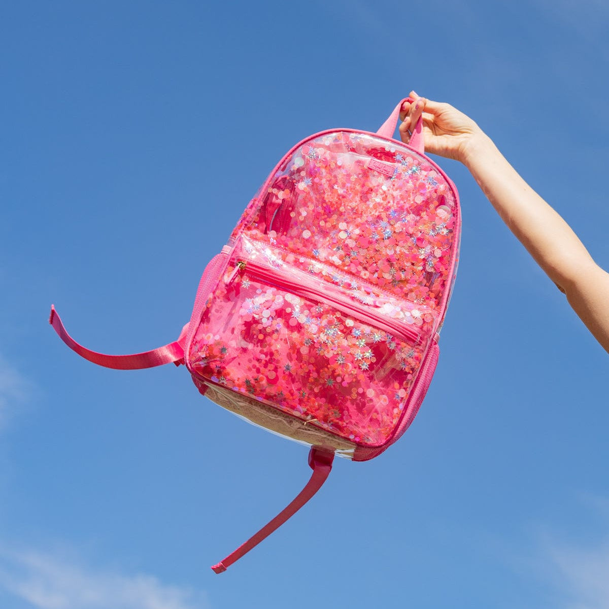 Sweet Tart Pink Confetti Clear Backpack held against a bright blue sky.