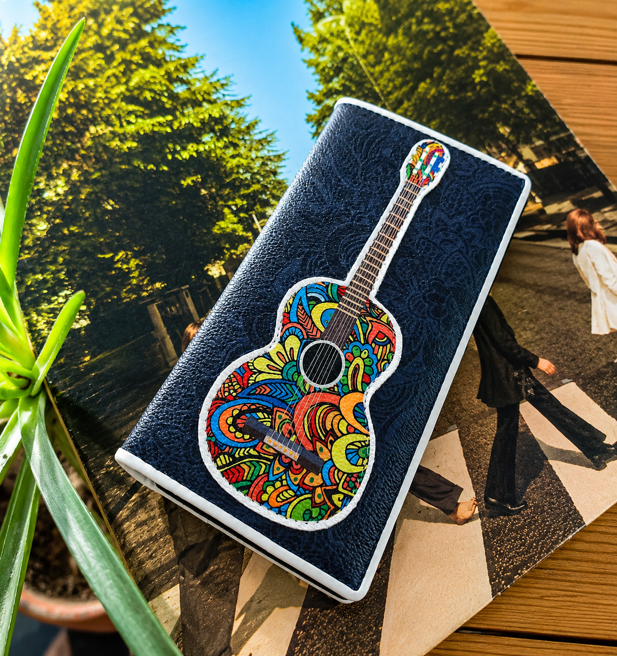 Women's wallet featuring a colorful acoustic guitar design displayed on a magazine with a decorative houseplant.