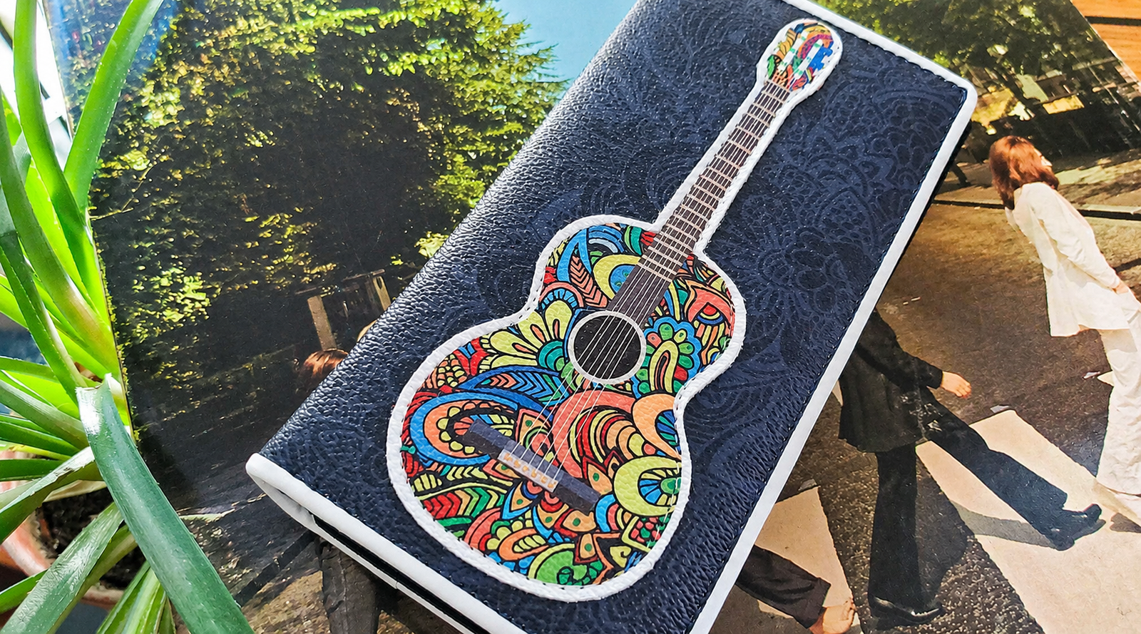 Women's wallet featuring a colorful acoustic guitar design displayed on a magazine with a decorative houseplant.