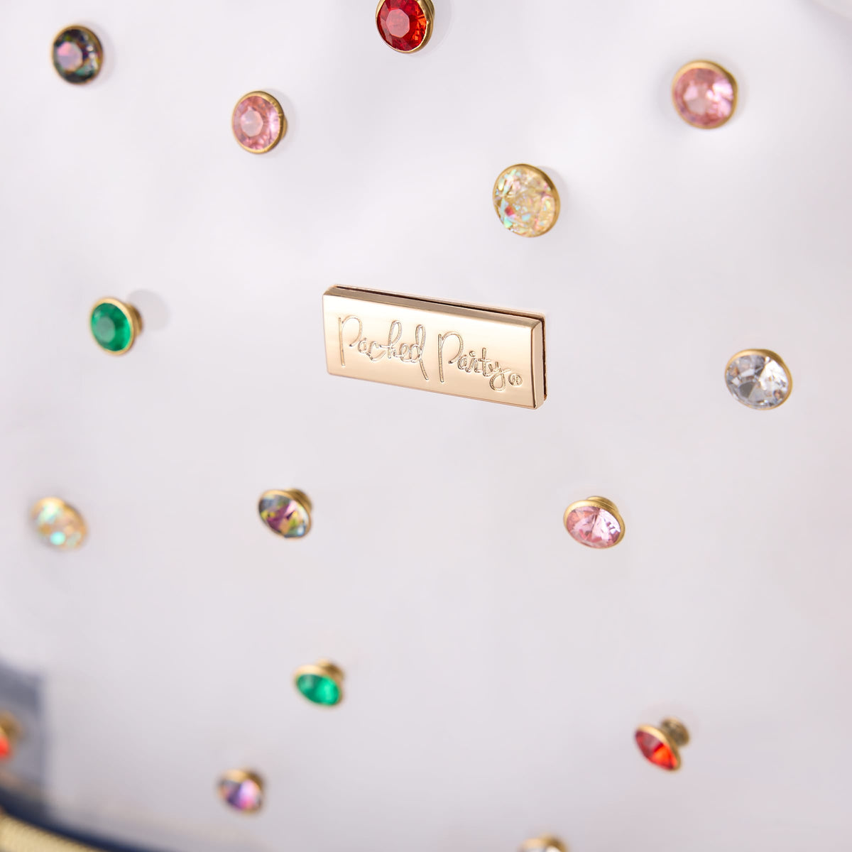 Close-up of colorful gemstone rivets and the Packed Party logo on the Clear Denim and Gems Backpack.