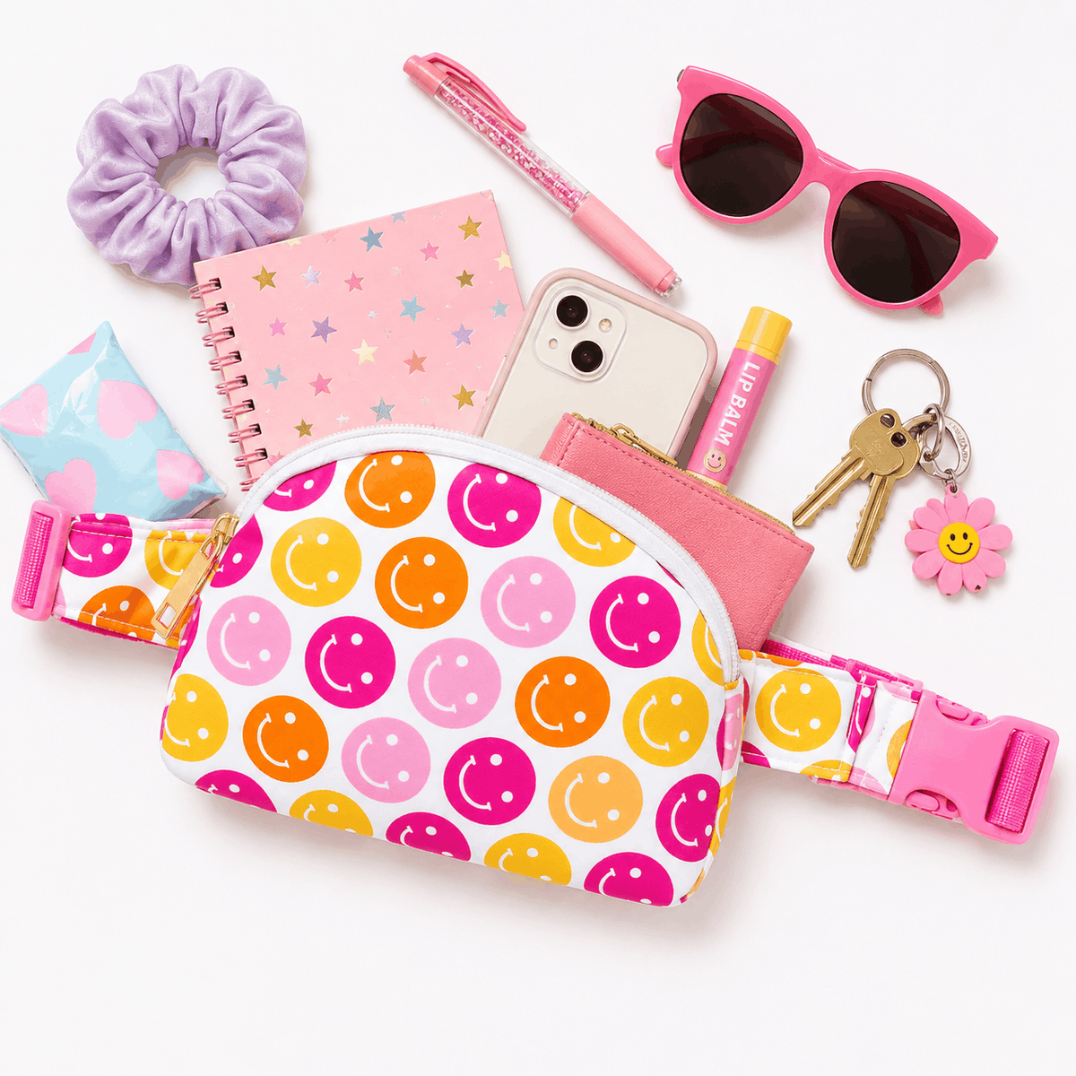 Flat lay of the Don't Worry Be Hippy belt bag with everyday essentials including a phone, wallet, sunglasses, notebook, lip balm, keys, and scrunchie