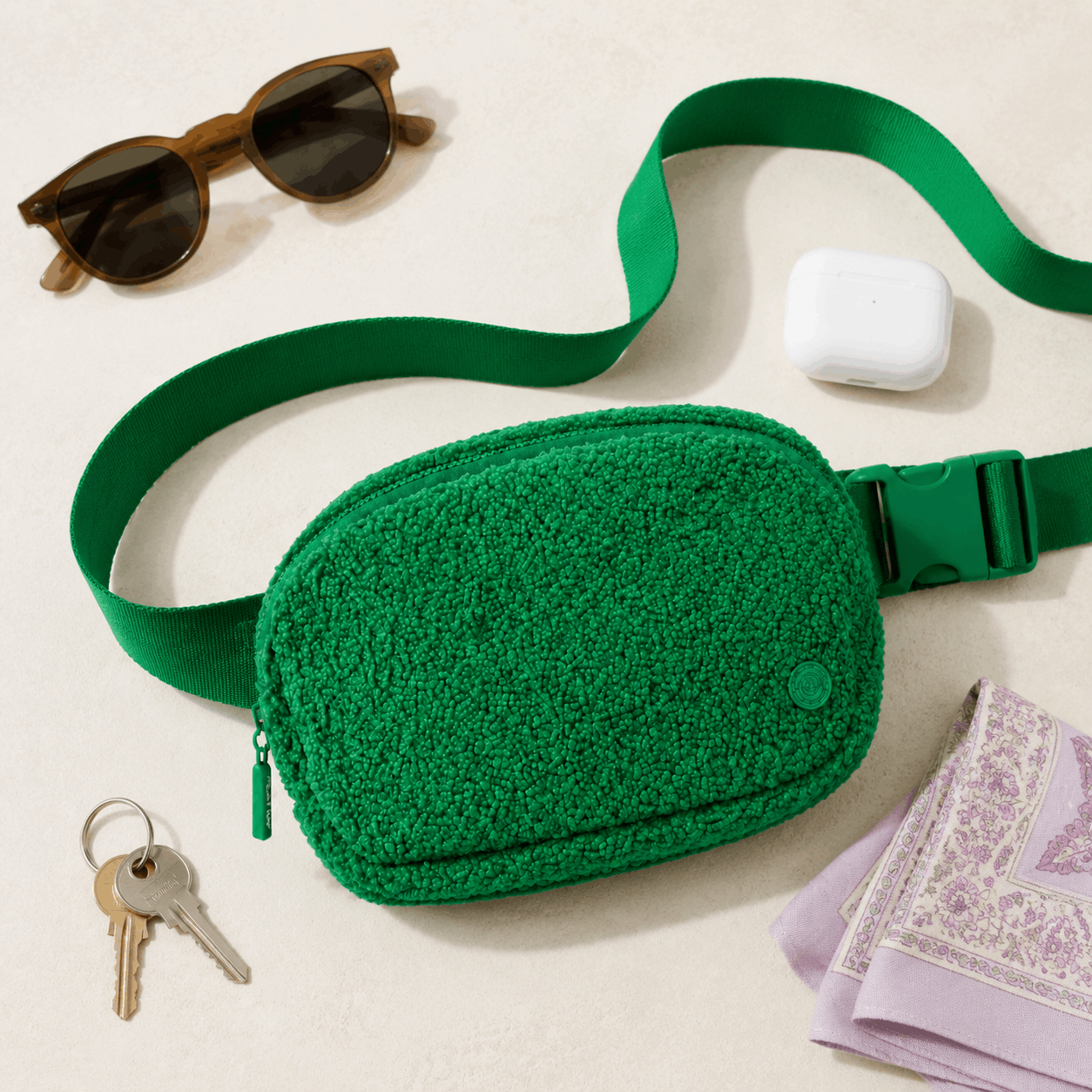 Green Fleece Belt Bag arranged with everyday essentials in a flat lay