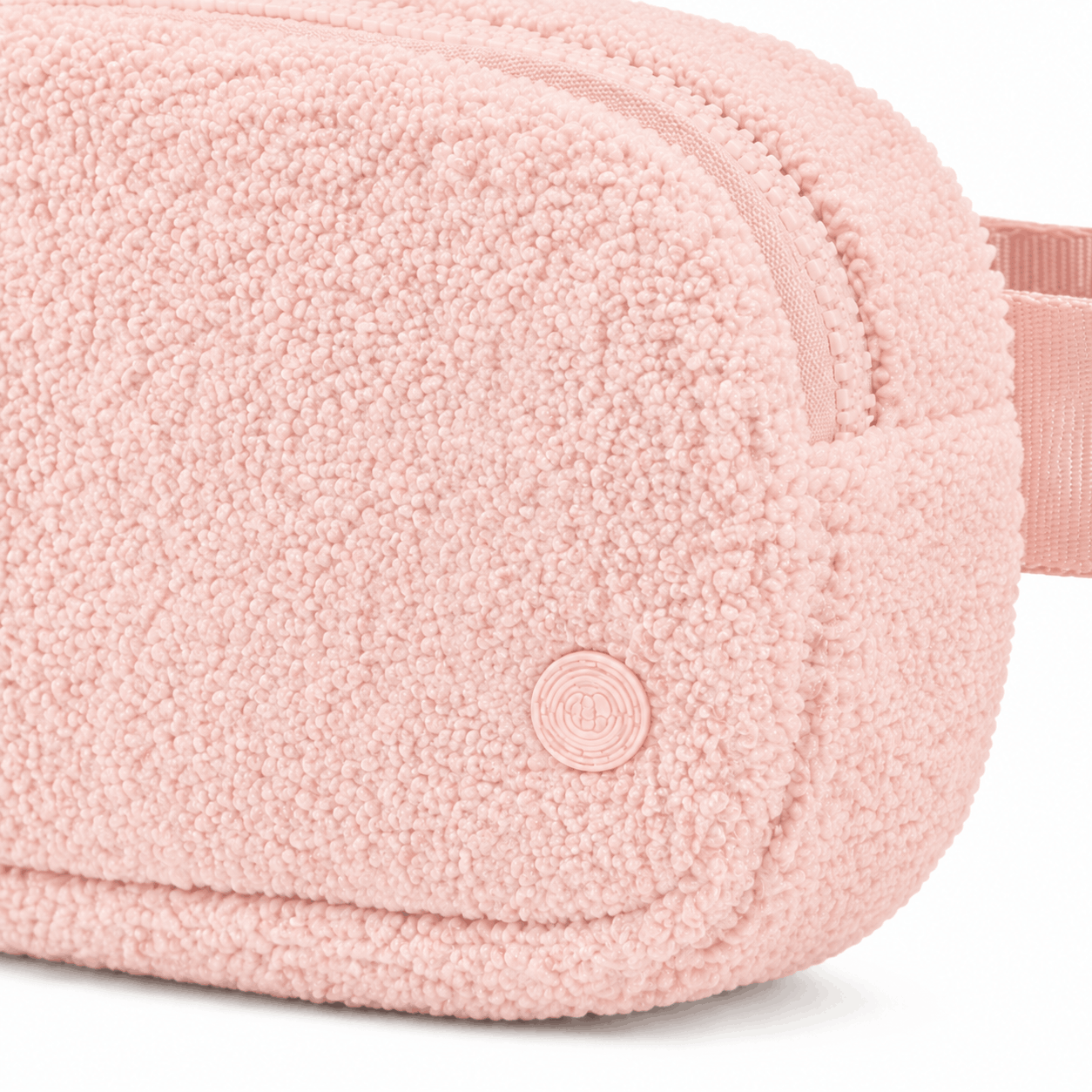 Close-up of light pink fleece texture, zipper, stitching, and circular emblem