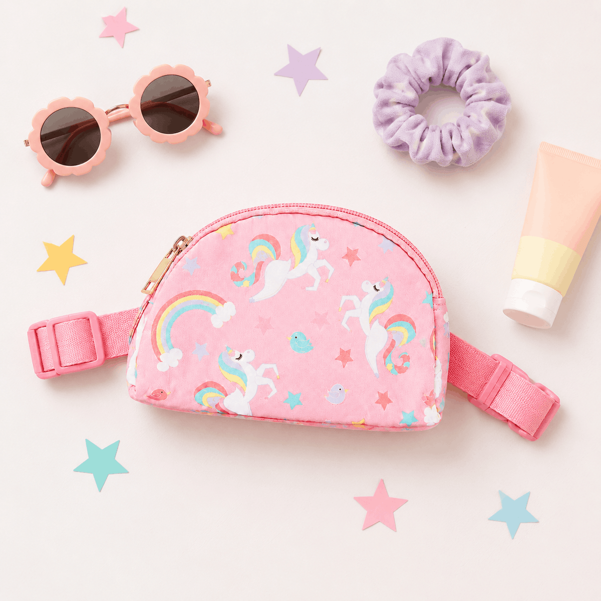Pink unicorn belt bag flat lay with sunglasses, scrunchie, and sunscreen
