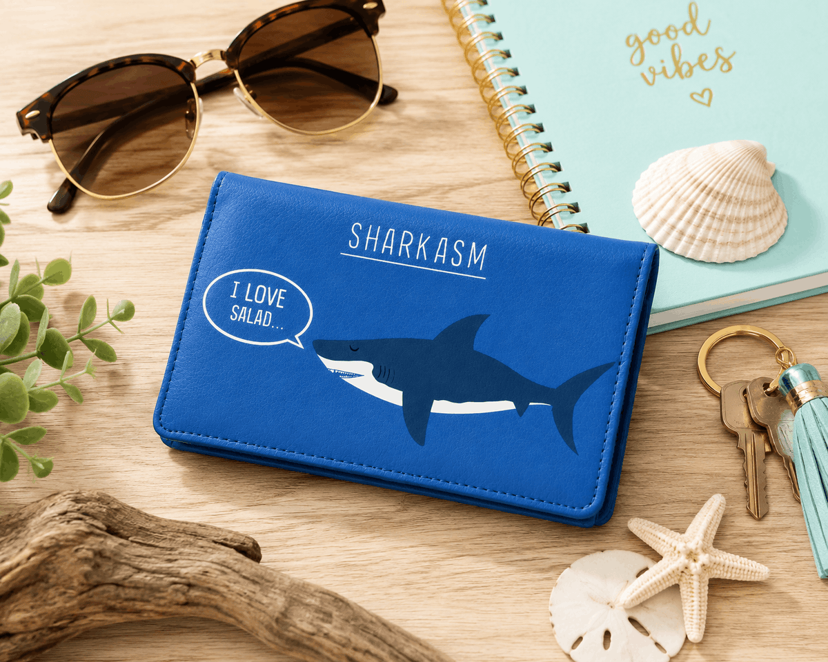 Sharkasm bifold wallet displayed with beach-inspired everyday accessories on a wooden table