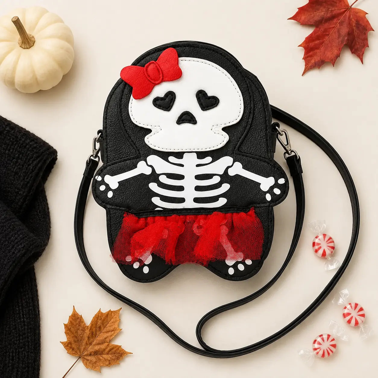 Skeleton girl crossbody bag flat lay with pumpkin, autumn leaves, and candy